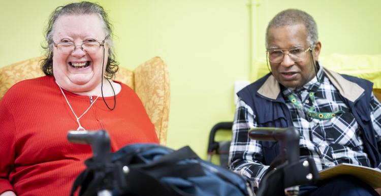 A woman with a walker and a man smiling in a residential setting.