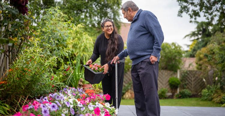 An older man using a walking stick and a younger woman gardening.