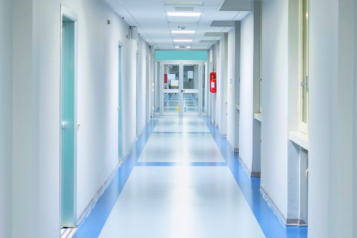 A blue and white hospital corridor with rooms off to each side.